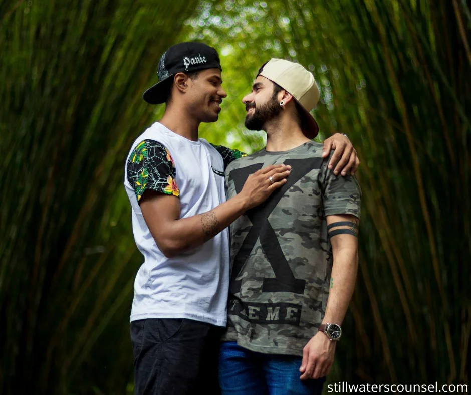 Two individuals wearing casual clothing stand facing each other, smiling, in an embrace under a canopy of tall, green bamboo.