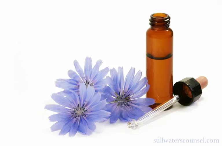 A small brown glass bottle with a dropper lying beside it is surrounded by three purple flowers with delicate petals. The scene is set against a white background.