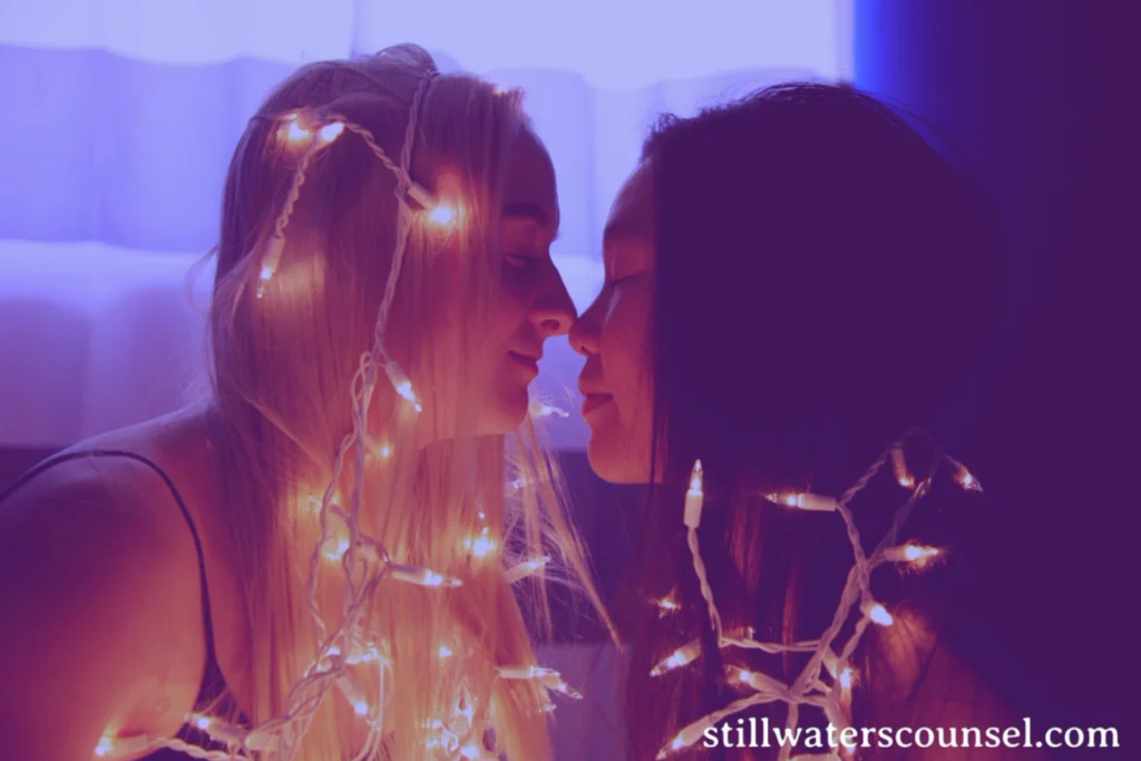 Two people facing each other closely with warm expressions, wrapped in glowing string lights. The background is softly lit with shades of blue and purple. The text stillwaterscounsel.com is at the bottom right corner.