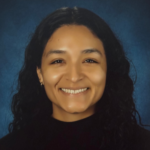 Smiling woman with long curly hair wearing a black top, posed against a blue background.